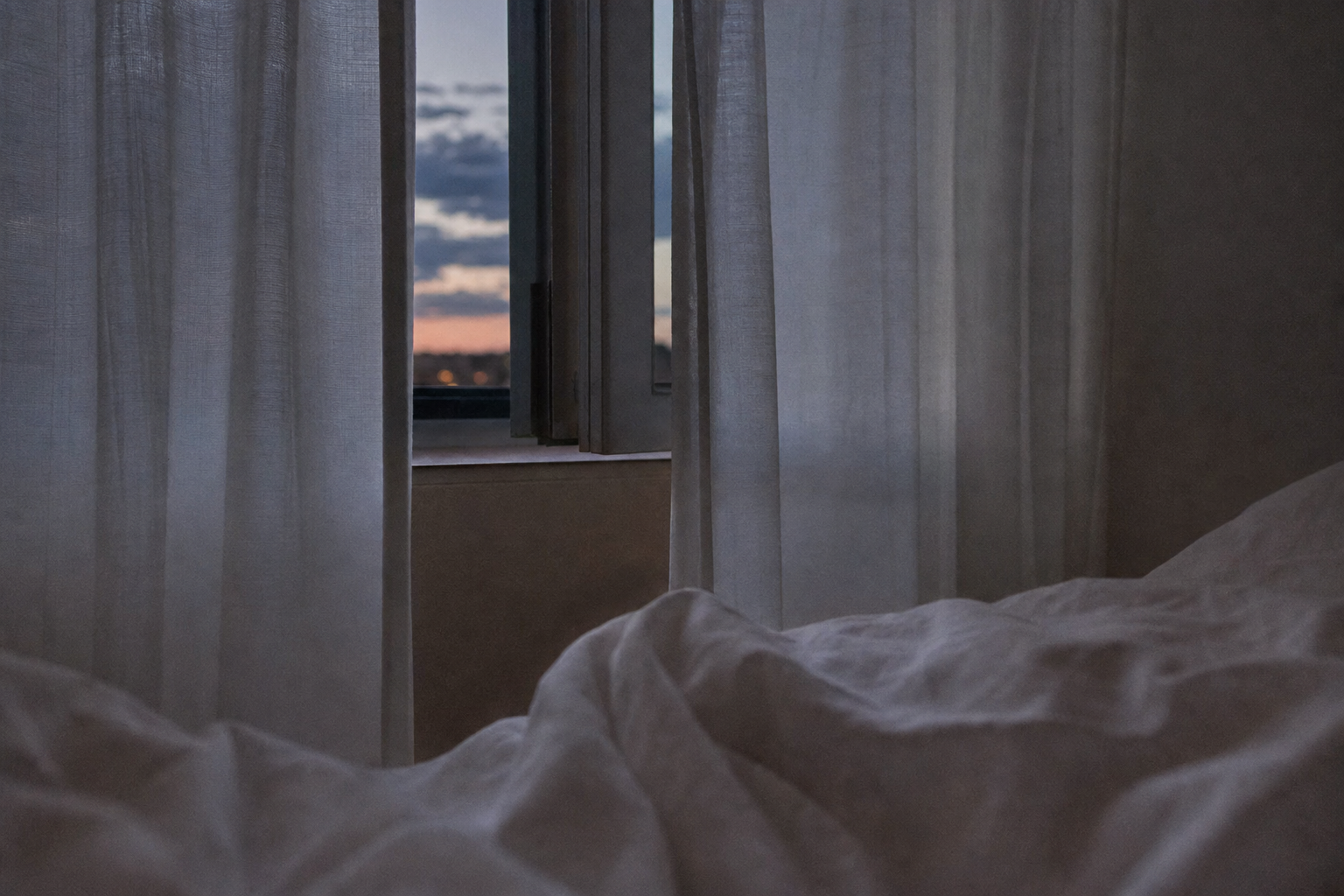 A closed bedroom at dusk, dim light through curtains — the Sleep Micro Environment where restoration is supposed to happen
